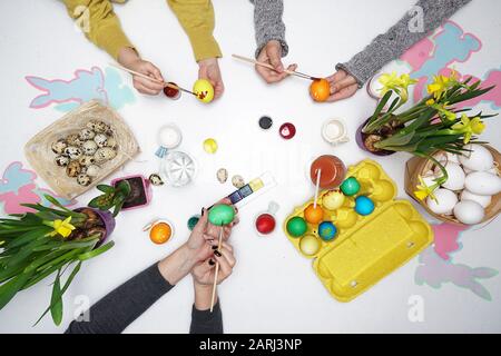 Vista dall'alto delle mani che dipinge le uova di Pasqua. Buona famiglia si prepara per la Pasqua. Uova di Pasqua su tavola bianca Foto Stock