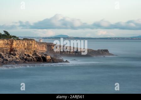 Le scogliere e l'Oceano Atlantico dal punto di riferimento Boca do Inferno a Cascais Portogallo nel pomeriggio sole con mare liscio che si infrangono su rocce con lunga esposizione Foto Stock
