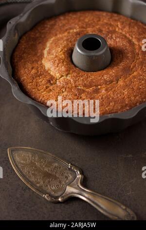 Bundt torta all'interno bundt pan con un server argento oltre ad esso, su sfondo grigio Foto Stock