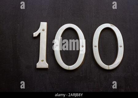 Numero 100 in cifre di metallo su sfondo nero su una porta di legno Foto Stock