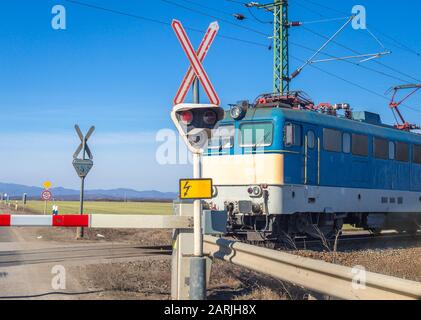 Semaforo rosso, barriera abbassata e treno elettrico in avvicinamento Foto Stock