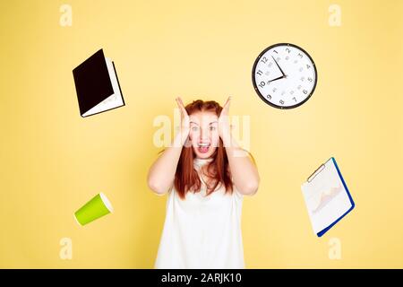 Scioccato, deadline.caucasico giovane donna ritratto su sfondo giallo studio, troppo compiti. Come gestire il tempo giusto. Concetto di lavoro, business, finanza, freelance, autogestione, pianificazione. Foto Stock