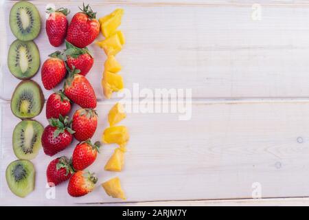 frutta tagliata a fette e intera: fragole, kiwi e mango su tavole di legno bianche Foto Stock