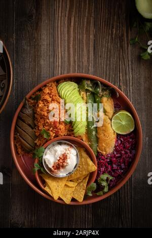 Ciotola vegetariana messicana contenente riso, peperoncini ripieni, lato barbabietola, avocado, panna acida e sottaceti Foto Stock