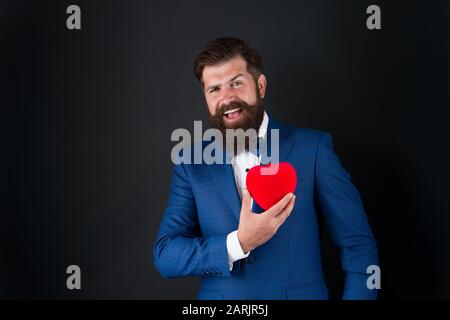 Assistenza sanitaria. Decorazione di giorno di San Valentino. Tuxedo uomo con cuore rosso. Festa di festa. Concetto di amore. Giornata mondiale del cuore. Brutale hipster barbuto in abito formale. Uomo d'affari in cravatta di prua. Attacco di cuore. Foto Stock