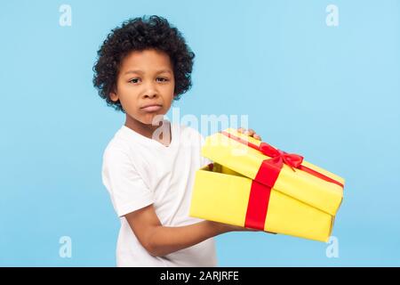 Ritratto di bambino divertente che tiene il contenitore del regalo unpacked e che guarda la macchina fotografica con il grimace insoddisfatto arrabbiato, bambino capriccioso dispiaciuto con Foto Stock