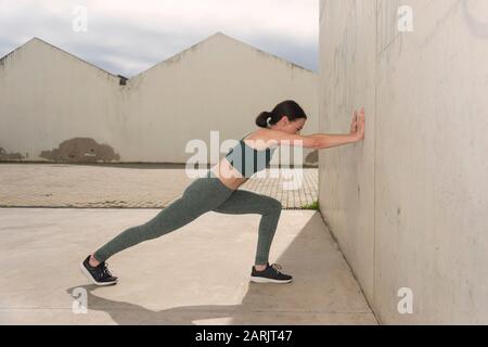 sportswoman stretching braccia e gambe, esercizi di riscaldamento, ambiente urbano concreto. Foto Stock