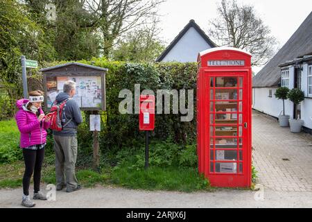Red British Telephone Box utilizzato come sede di prestito di libri nel piccolo villaggio di Abington Pigotts, Cambridgeshire, Regno Unito. Due escursionisti alla ricerca di dire Foto Stock