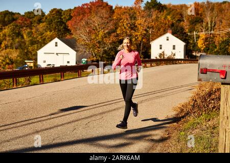 Una donna corre lungo una strada di campagna in un giorno di autunno. Foto Stock