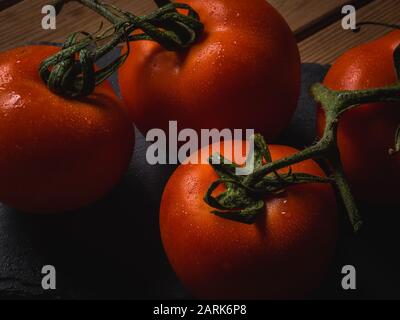 Mazzo di pomodori rossi su un tavolo con gocce di acqua fredda sopra di loro. Foto Stock