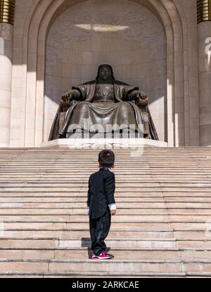 Ragazzo su gradini che guarda la statua di Genghis Khan, luogo del governo, Piazza Sükhbaatar, Ulaanbaatar, Mongolia Foto Stock