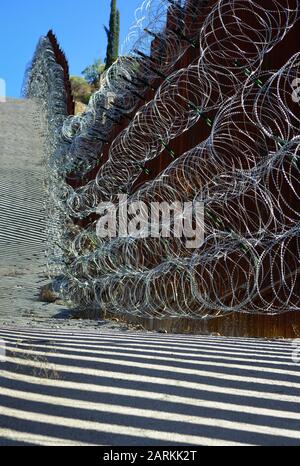 Vista della recinzione di confine internazionale USA/Messico con filo di rasoio in salita con il Messico dall'altro lato della recinzione da Nogales, AZ, USA, Foto Stock