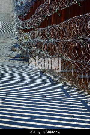 Vista astratta della recinzione di confine internazionale USA/Messico con filo di rasoio con luce e ombre drammatiche a Nogales, AZ, USA, Foto Stock