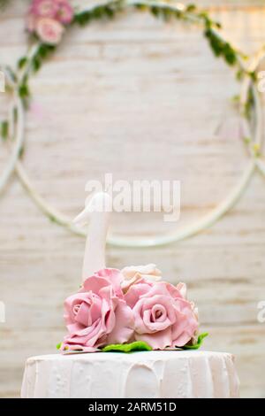 Cima di torta di lusso adornata con rose e una candela bianca di un anno su uno sfondo di legno chiaro. Concetto di celebrazione. Foto Stock
