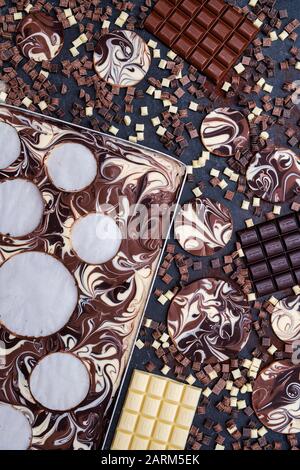 Dischi di cioccolato marmorizzato tagliati da un vassoio con barrette di cioccolato e pezzi su un fondo di ardesia Foto Stock