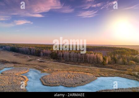 Vista aerea della campagna e del ruscello ghiacciato in serata al tramonto. Bellissimo paesaggio naturale con cielo nuvoloso. Foto Stock