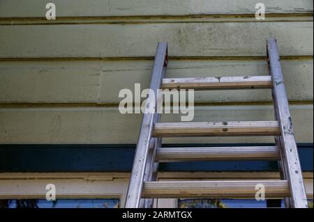 Una casa in legno, dipinta di verde, ha una scala appoggiata contro di essa Foto Stock