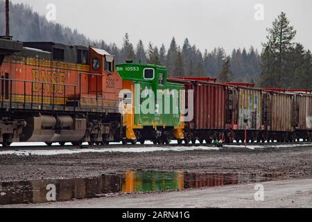 Una cabina della Burlington Northern BNSF Railroad e una linea di box car dietro una locomotiva elettrica BNSF diesel, sulle piste nella città di Troy, Montana. Foto Stock