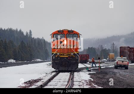 Una locomotiva BNSF nera, gialla e arancione, che gira al minimo sulle piste nella città di Troy, Montana. Foto Stock