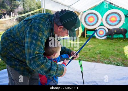 Un ragazzo in Spiderman vestito tiene arco e freccia come un uomo adulto lo insegna a sparare ai bersagli al Steelhead Festival al lago Sonoma California. Foto Stock