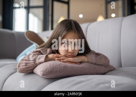 Bambina con un triste sguardo sdraiata sul divano. Foto Stock