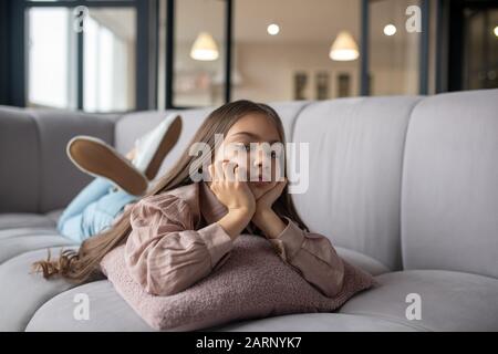 Piccola ragazza triste sdraiata su un divano a casa. Foto Stock