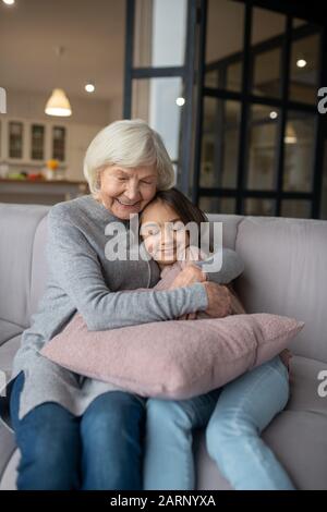 Nonna abbracciando strettamente nipote seduto sul divano. Foto Stock