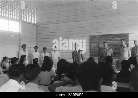 Dintorni Fort de Kock un uomo indonesiano si rivolge ai bambini delle scuole superiori in una stanza di legno. A destra ci sono soldati olandesi e funzionari governativi. Sulla sinistra quattro uomini indonesiani in abbigliamento leggero. Sul muro una lavagna con testo Data: 14 febbraio 1949 luogo: Indonesia, Indie orientali olandesi, Sumatra Foto Stock
