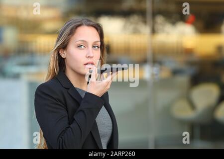 Un dirigente meraviglioso che utilizza il riconoscimento vocale sul telefono cellulare a piedi lungo la strada accanto a un ufficio Foto Stock