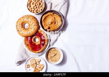 Bagels fatti in casa con noccioline di paleo naturale e burro cremoso cashew e marmellata su sfondo bianco. Sana colazione brunch concetto. Vista dall'alto Foto Stock