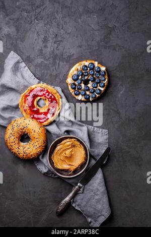 Varietà di bagel con diversi condimenti e noce paleo naturale arachidi burro cremoso su fondo grigio scuro. Sana colazione brunch concetto Foto Stock