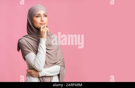 Ritratto di donna islamica millenaria pensierosa in velo su sfondo rosa Foto Stock