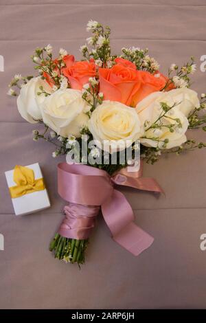 Bouquet di rose bianche e arancioni avvolte da un fiocco di raso viola sul letto. Concetto di impegno e matrimonio. Foto Stock