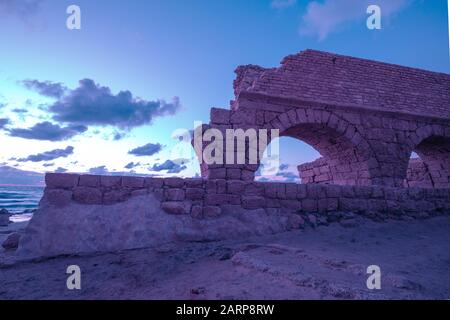 Acquedotto nella città antica Cesarea al tramonto. Colore viola alla moda Foto Stock