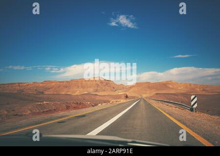 Guida di un'auto sulla strada di montagna Israele. Paesaggio desertico. Strada vuota. Vista dall'auto del paesaggio montano in una giornata di sole. Israele Foto Stock