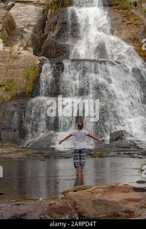 Diyaluma, Haputale, Sri Lanka. 2019 22 novembre: Giovane donna Blonde nel ritorno nella giornata del sole nella cascata tropicale cade dalla scogliera di montagna fino a. Foto Stock