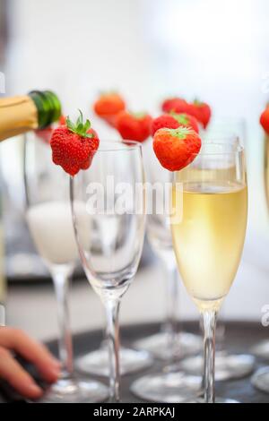 Spumante o champagne e fragola su uno sfondo sfocato che viene versato dalla bottiglia durante una sorta di festa o celebrazione come un matrimonio, un giorno di borthday o un anno nuovo Foto Stock