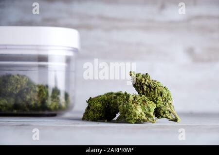 Un contenitore sigillato ad aria e gemme di fiori di marijuana ricreativa contro uno sfondo di pietra bianca dopo che l'Illinois passa una legge per legalizzare le vendite di alghe Foto Stock