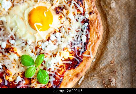 Dettaglio di una pizza con uova, formaggio ed erbe. Scena rustica e luce drammatica. Foto Stock