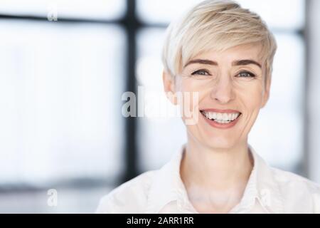 Businesswoman Di Mezza Età Sorridente Alla Camera Che Posa In Ufficio Moderno Foto Stock