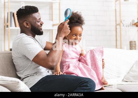 Papà nero felice spazzolando la sua bella figlia piccola Foto Stock