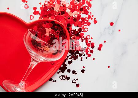 Cena di San Valentino. Piastra a cuore rossa con champagne e confetti Foto Stock