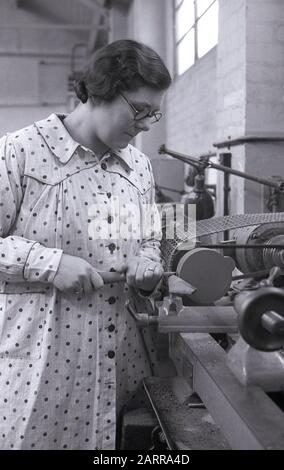 1948, storica, una giovane donna che indossa un capo a maniche lunghe macchiato o pinafore, in una lezione serale di lavorazione del legno, in piedi su un banco di lavoro per affilare un utensile manuale, Londra, Inghilterra, Regno Unito. C'è stato un notevole aumento dell'educazione degli adulti e l'enfasi nell'apprendimento di nuove competenze per le persone nel Regno Unito post-seconda guerra mondiale. Foto Stock