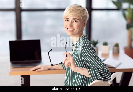 Felice Businesswoman Di Mezza Età Seduto Alla Scrivania In Ufficio Moderno Foto Stock