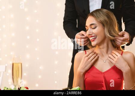 Uomo Che Mette Golden Necklace Sul Collo Della Ragazza A Data In Ristorante Foto Stock