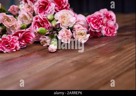 Bouquet di garofani rosa, bouquet di regali su sfondo ligneo. Concezione di cartoline con l'aggiunta di testo. Spazio di copia . Foto Stock