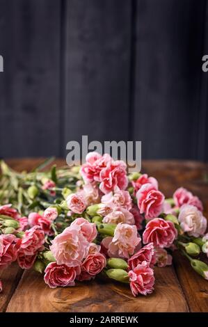 Bouquet di garofani rosa, bouquet di regali su sfondo ligneo. Concezione di cartoline con l'aggiunta di testo. Spazio di copia . Foto Stock