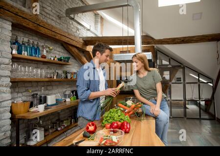 Giovane coppia trendy peeling e taglio verdure dal mercato in cucina rustica Foto Stock