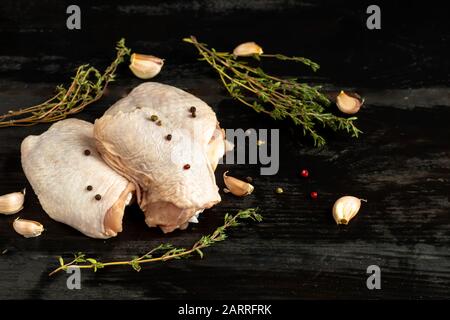 Su carta marrone, cosce fresche di pollo senza pelle, accanto ai funghi, con pomodori, cipolle rosse e timo. Ricetta del piatto. Ingredienti. Su un legno nero Foto Stock