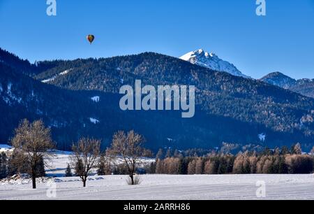 In una splendida mattinata invernale un pallone d'aria calda passa sopra la valle di Dobbiaco Foto Stock